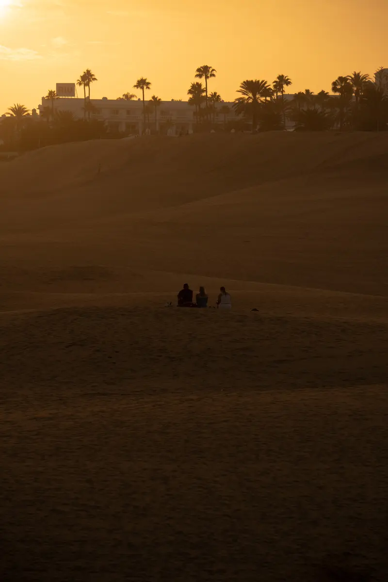 Tre persone sedute nella duna al tramonto, sotto l'insegna di un hotel