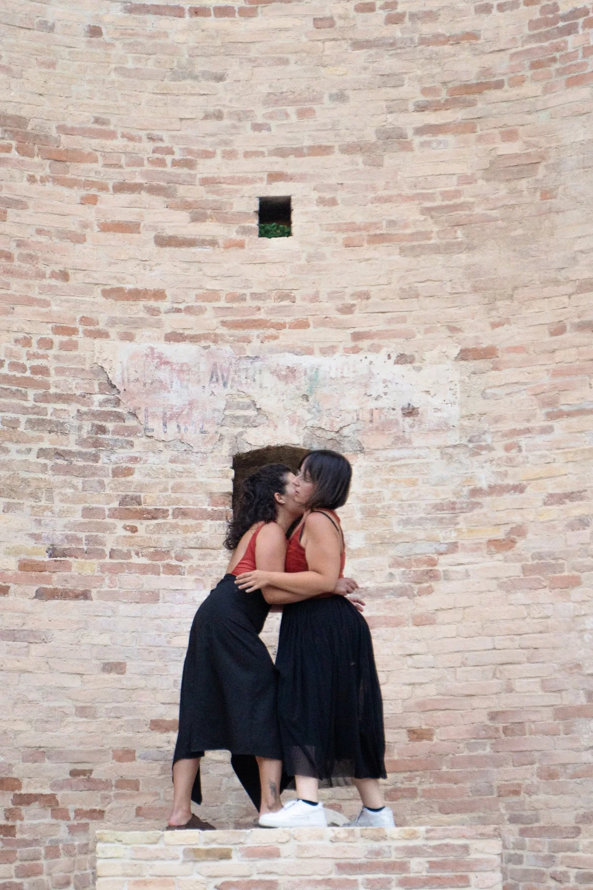 Due performer abbracciate davanti a un muro di mattoni