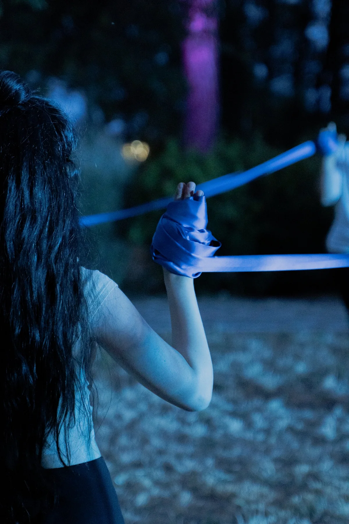 Di notte, una performer di spalle con la mano avvolta in un nastro blu teso