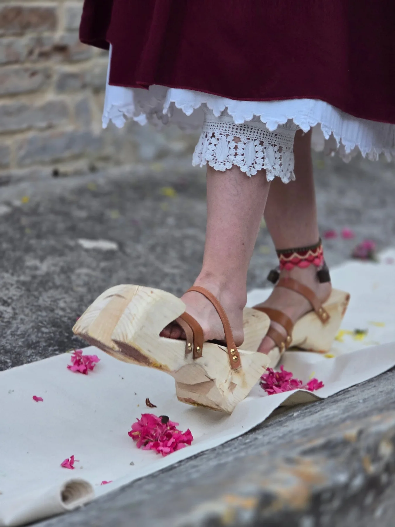 Piedi in grandi zoccoli di legno su un telo bianco cosparso di petali fucsia