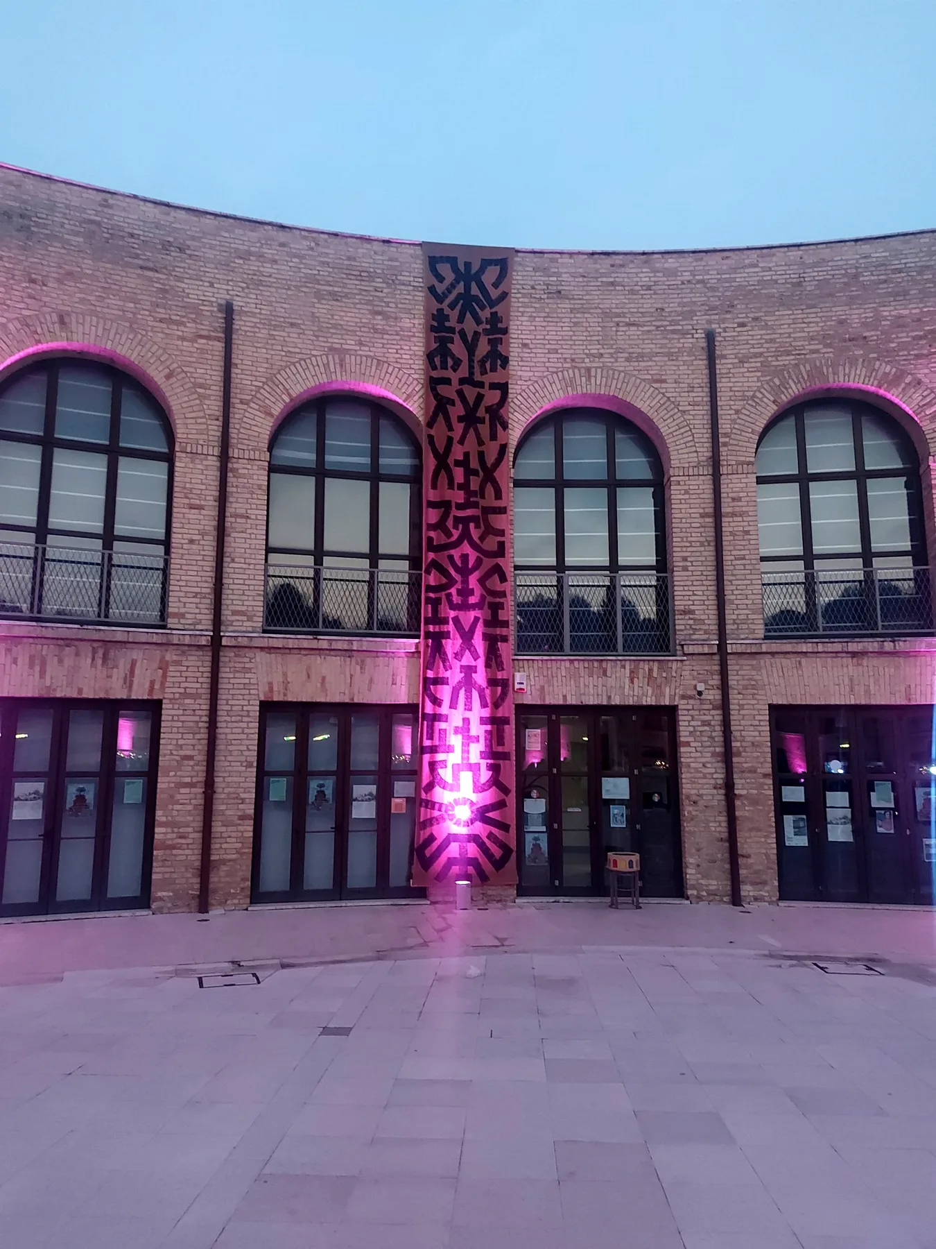 Un lungo drappo con segni neri appeso alla facciata in mattoni dell'Aurum, illuminato di rosa