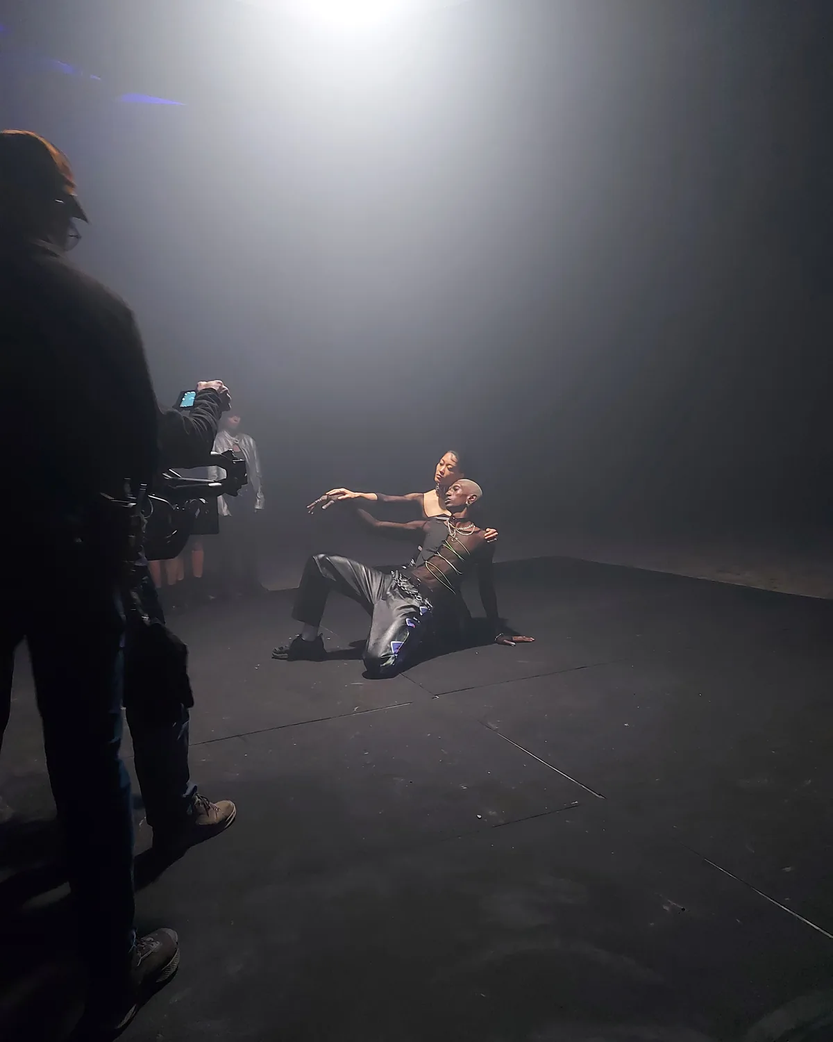 Una ballerina nel fumo, illuminata dall'alto; a sinistra l'operatore con la camera