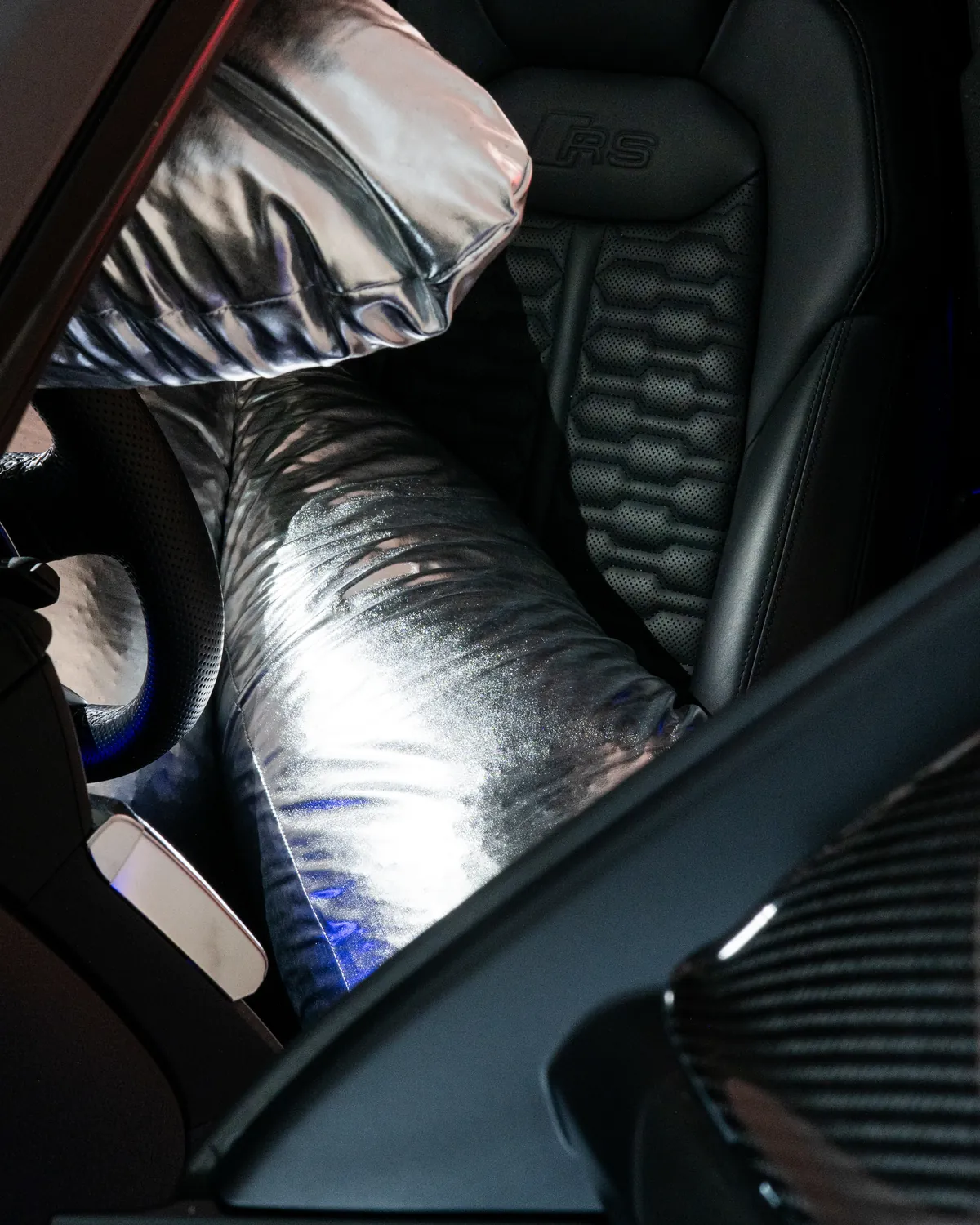 Una scultura argentata imbottita appoggiata sul sedile di un'auto, in luce blu